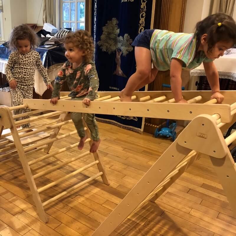 Three young children playing on a wooden indoor climbing triangle for motor skill development