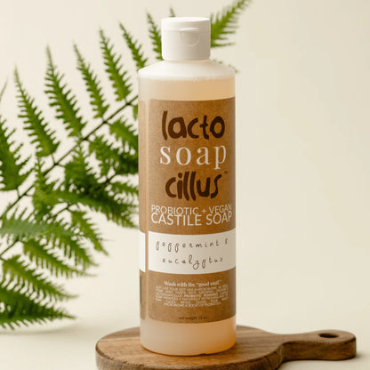 16 oz bottle of probiotic vegan castile soap peppermint eucalyptus on wooden board with fern