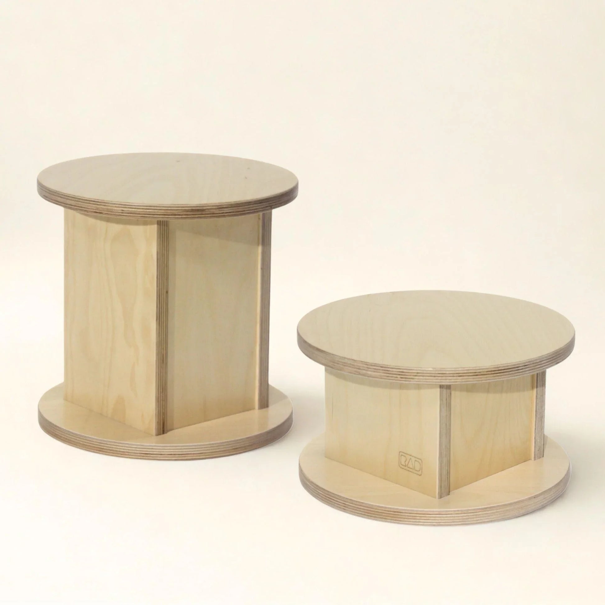 Two round wooden children's stools with light wood finish on a plain background