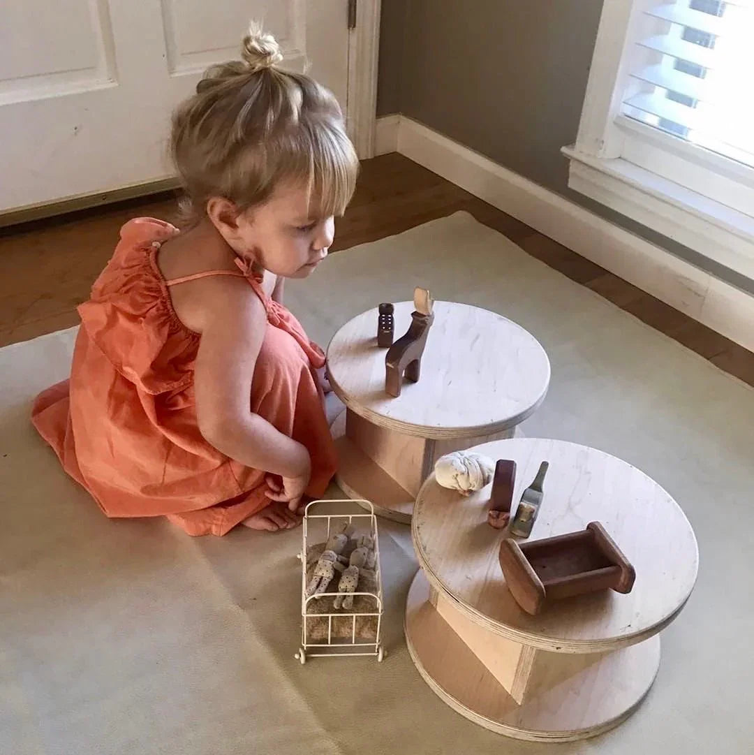 Young child in orange dress playing with wooden sensory toys on round wooden stools indoors