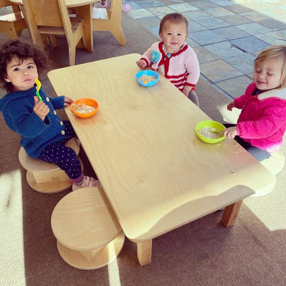 Three toddlers eating cereal at a low sensory-friendly wooden table with stools