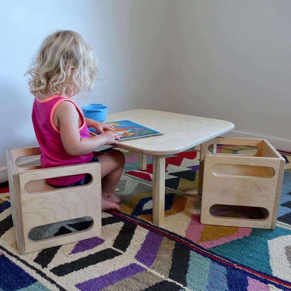 Child using Montessori cube chair and table set on a colorful rug, reading a book.