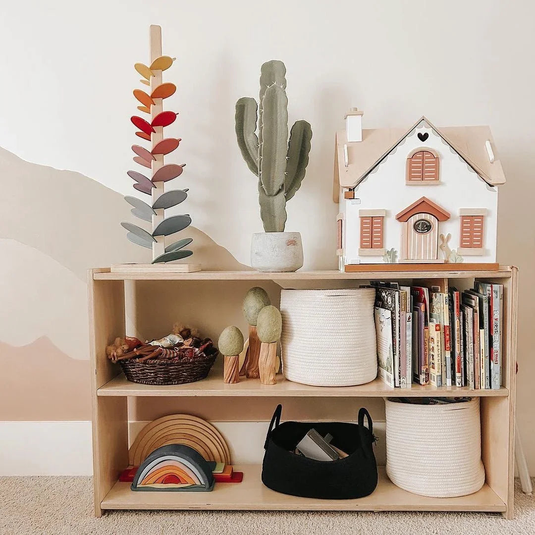 Wooden shelf with sensory toys, baskets, books, rainbow stacker, and dollhouse in a cozy room.