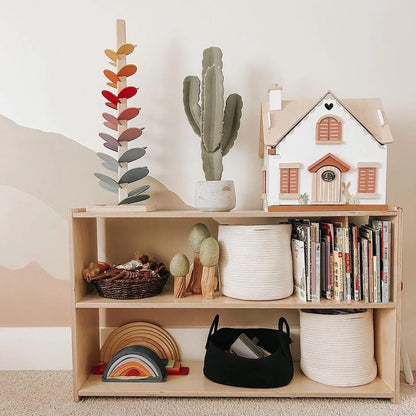 Wooden shelf with sensory toys, baskets, books, rainbow stacker, and dollhouse in a cozy room.