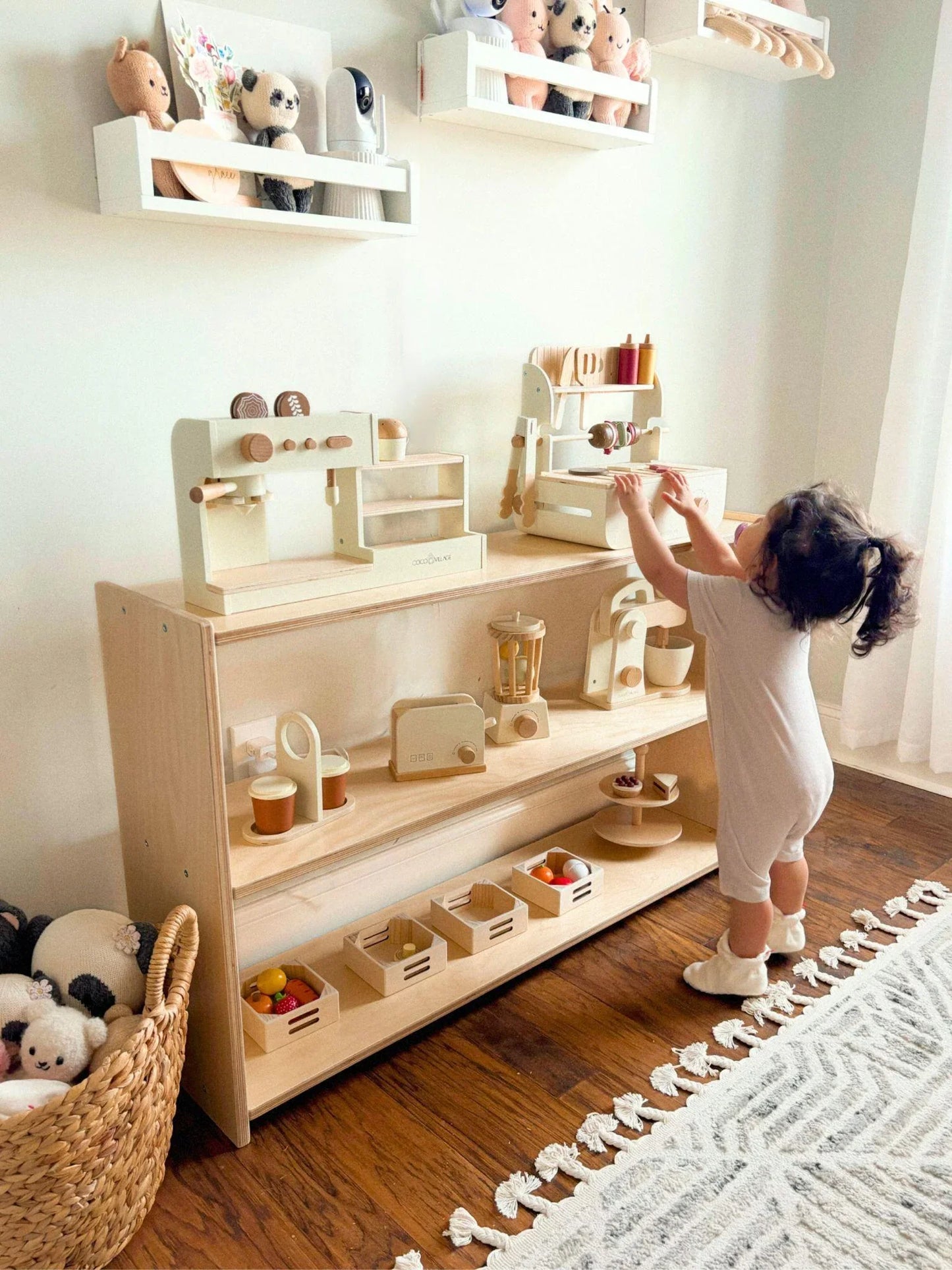 Toddler playing in a sensory-friendly room with wooden kitchen toys and plush stuffed animals.