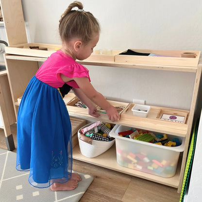 Young child in colorful dress organizing sensory learning toys on wooden Montessori shelf.