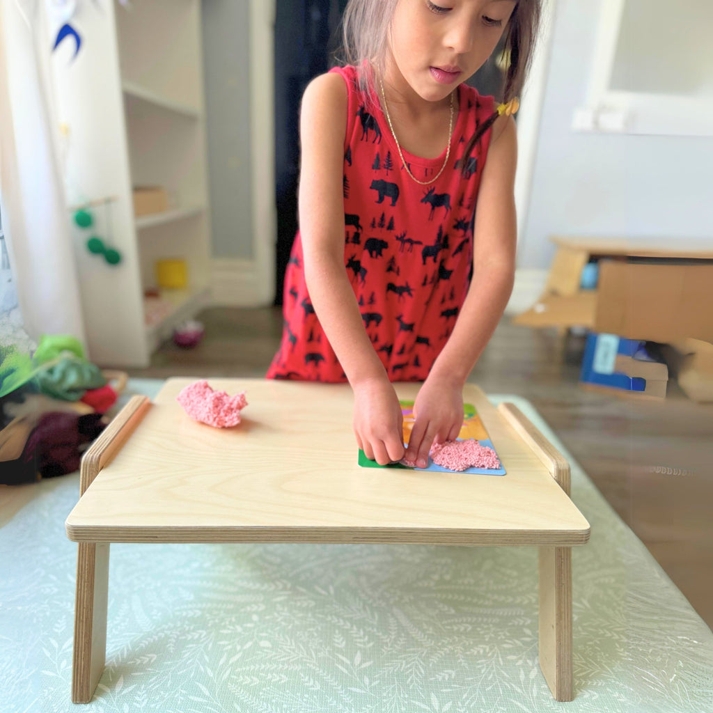 Child playing with colorful blocks on a small wooden table in a room.