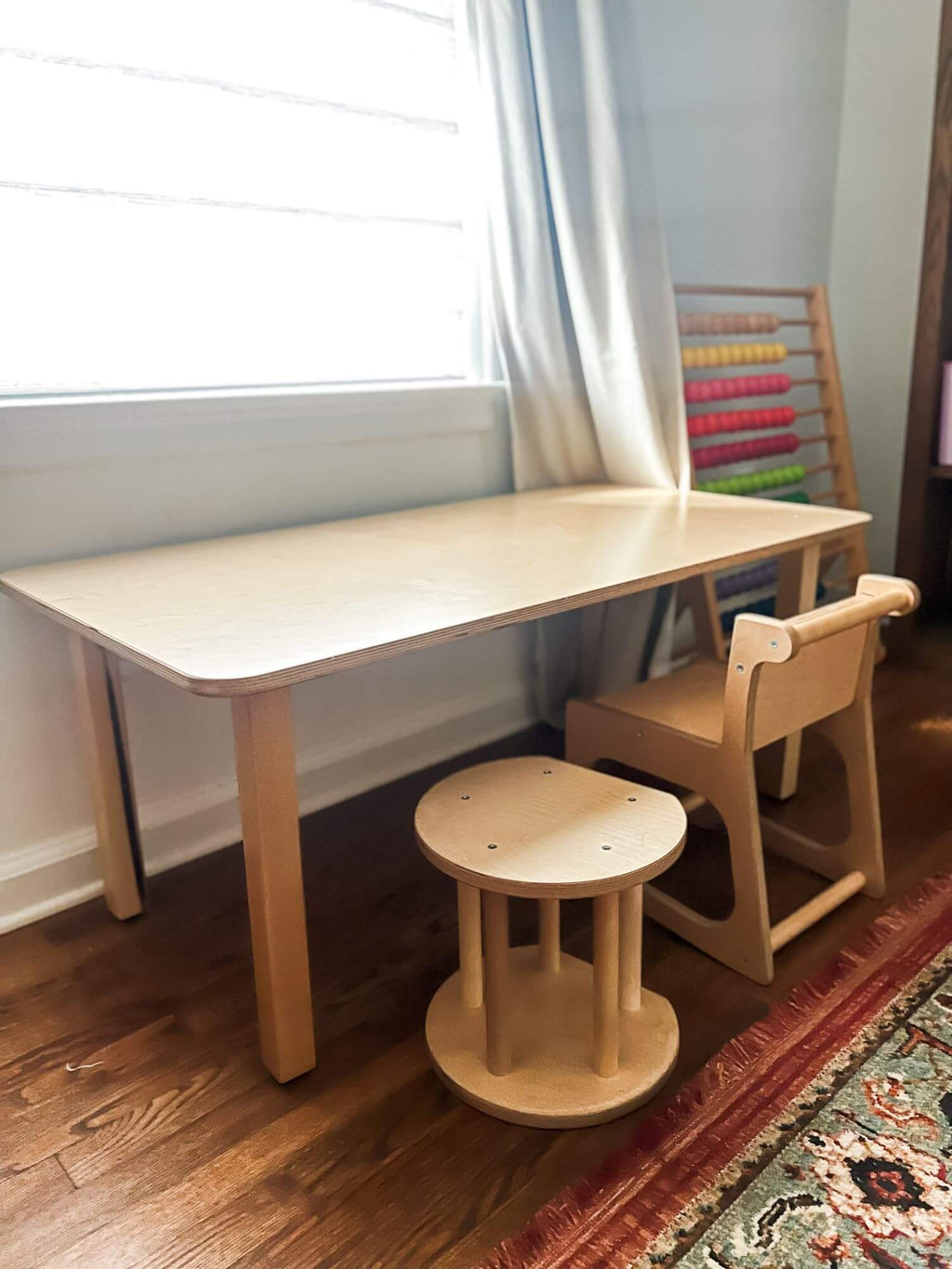 Wooden children's table and chairs in a room with a window and rug.