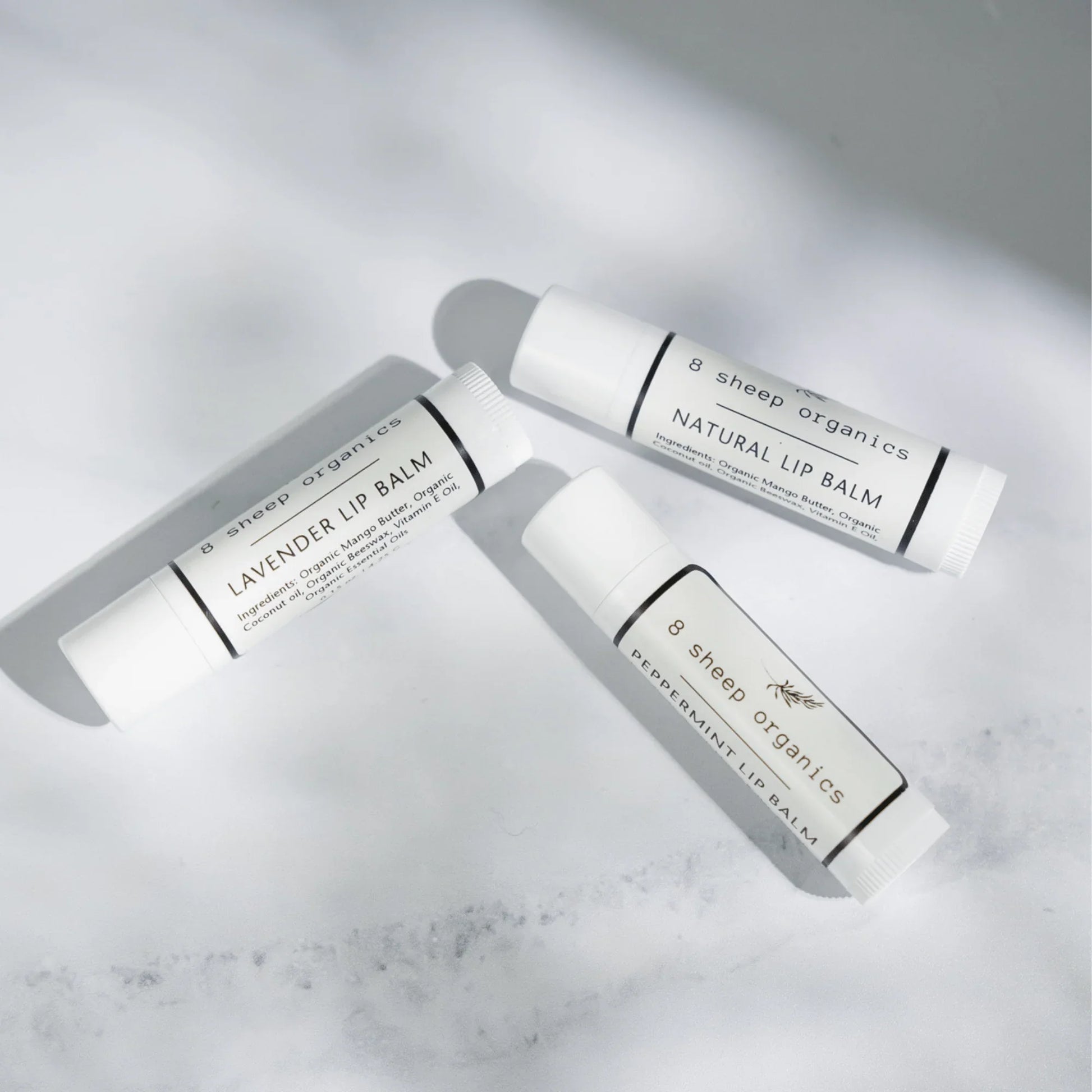 Three 8 Sheep Organics lip balm tubes—lavender, natural, and peppermint—on white surface.