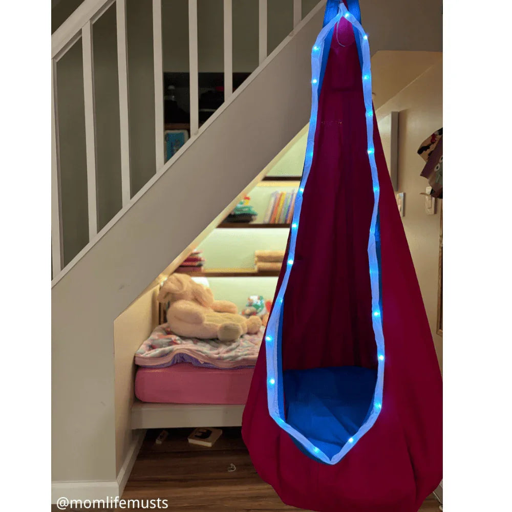 Sensory pod swing with blue LED lights hanging by a cozy reading nook under stairs