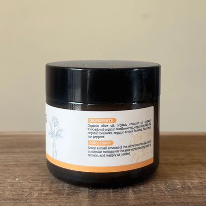 Brown jar of natural pain relieving salve on a wood surface, label with ingredients visible.