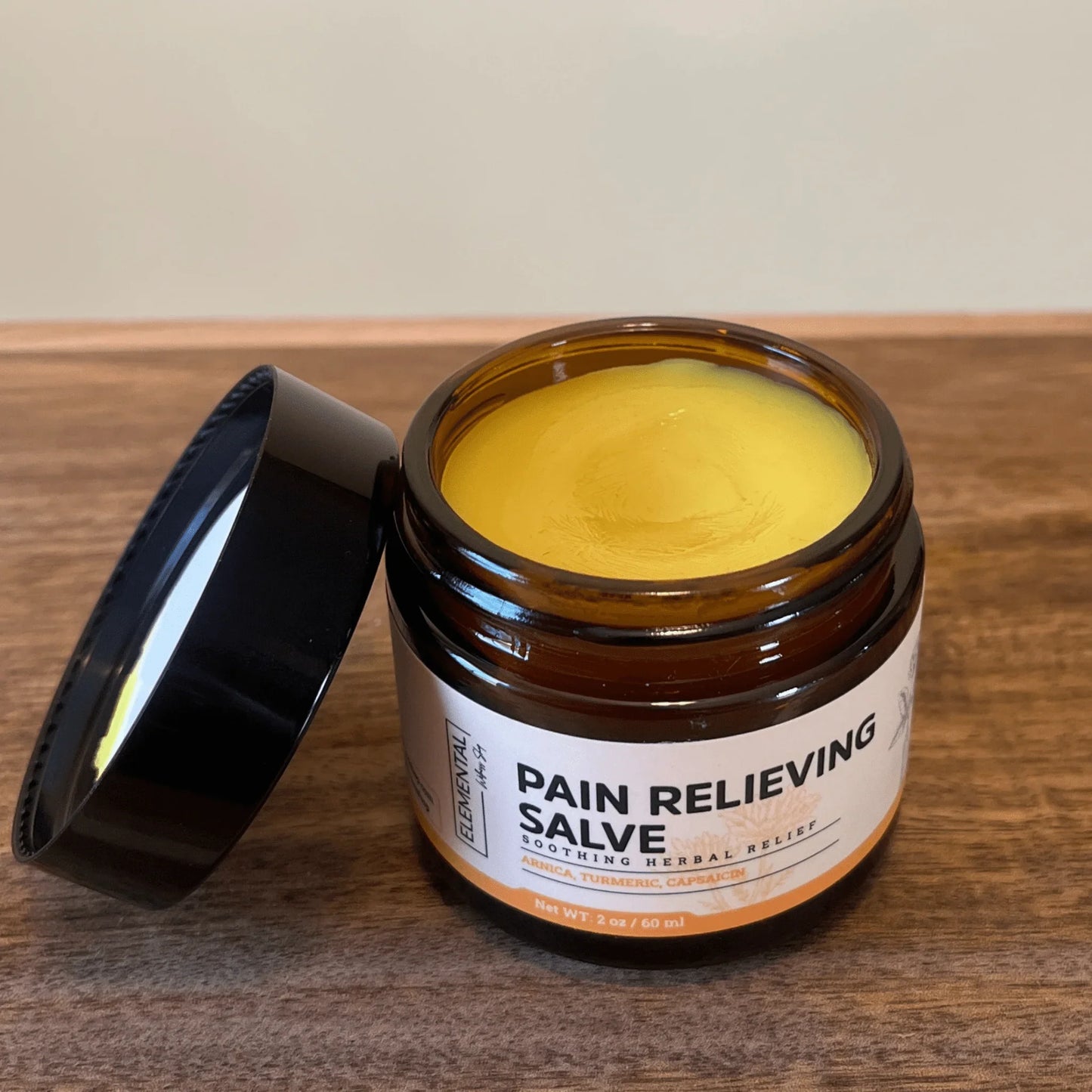 Open jar of pain relieving salve with herbal ingredients on wood surface