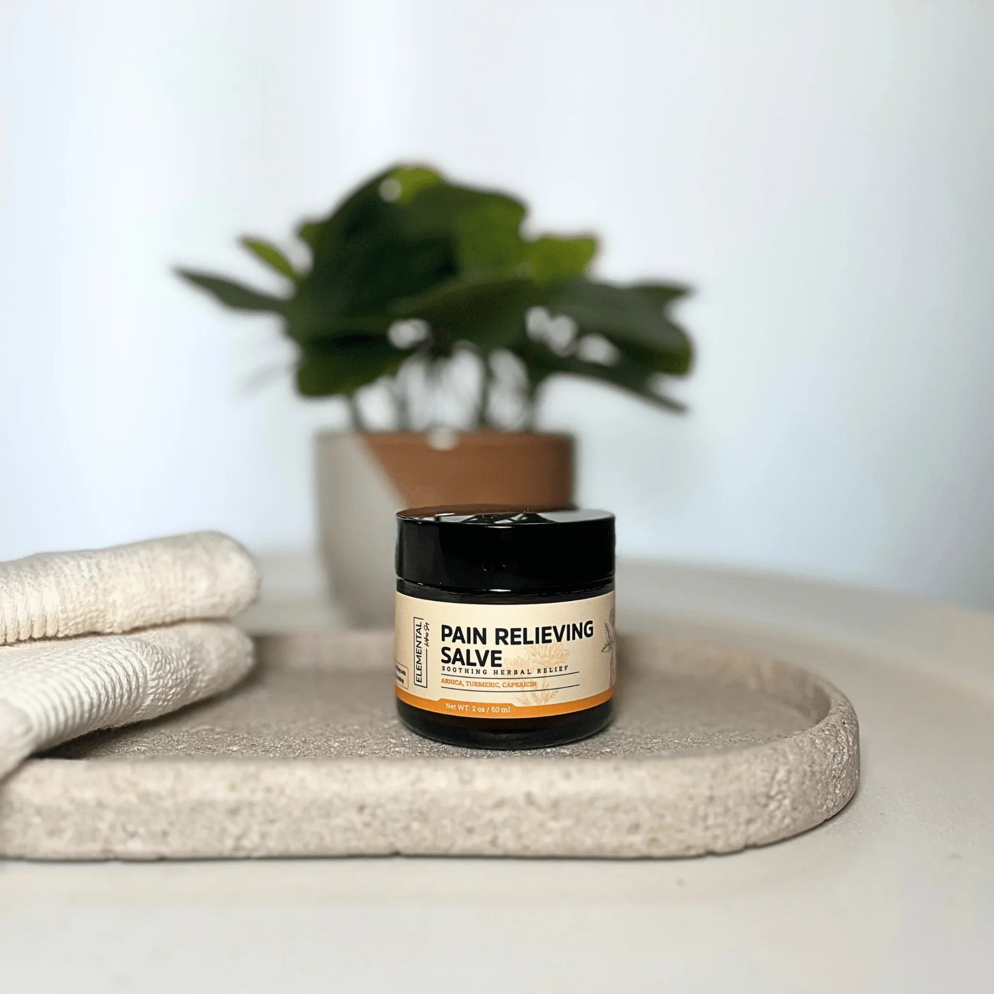 Pain relieving salve jar on tray with towels, herbal remedy for natural pain relief