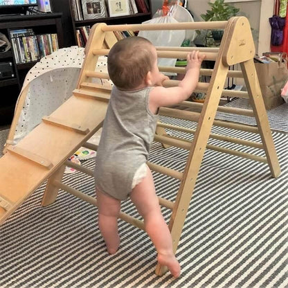 Baby climbing a wooden Pikler triangle indoor climbing toy on a striped rug