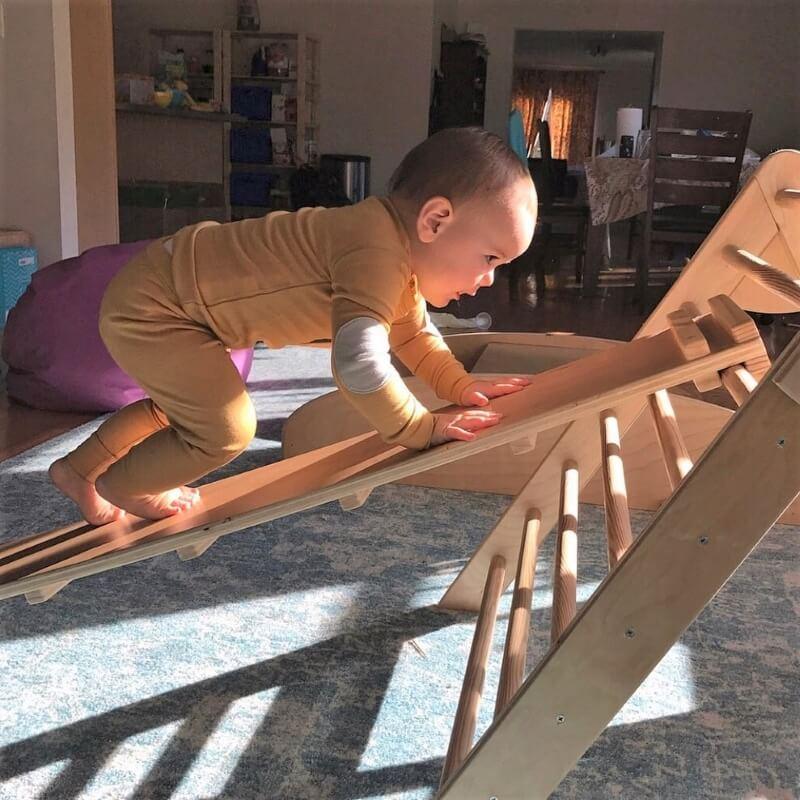 Baby climbing on wooden Pikler triangle sensory playset indoors