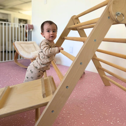 Baby in sensory pajamas playing on wooden climbing triangle in a safe indoor playroom