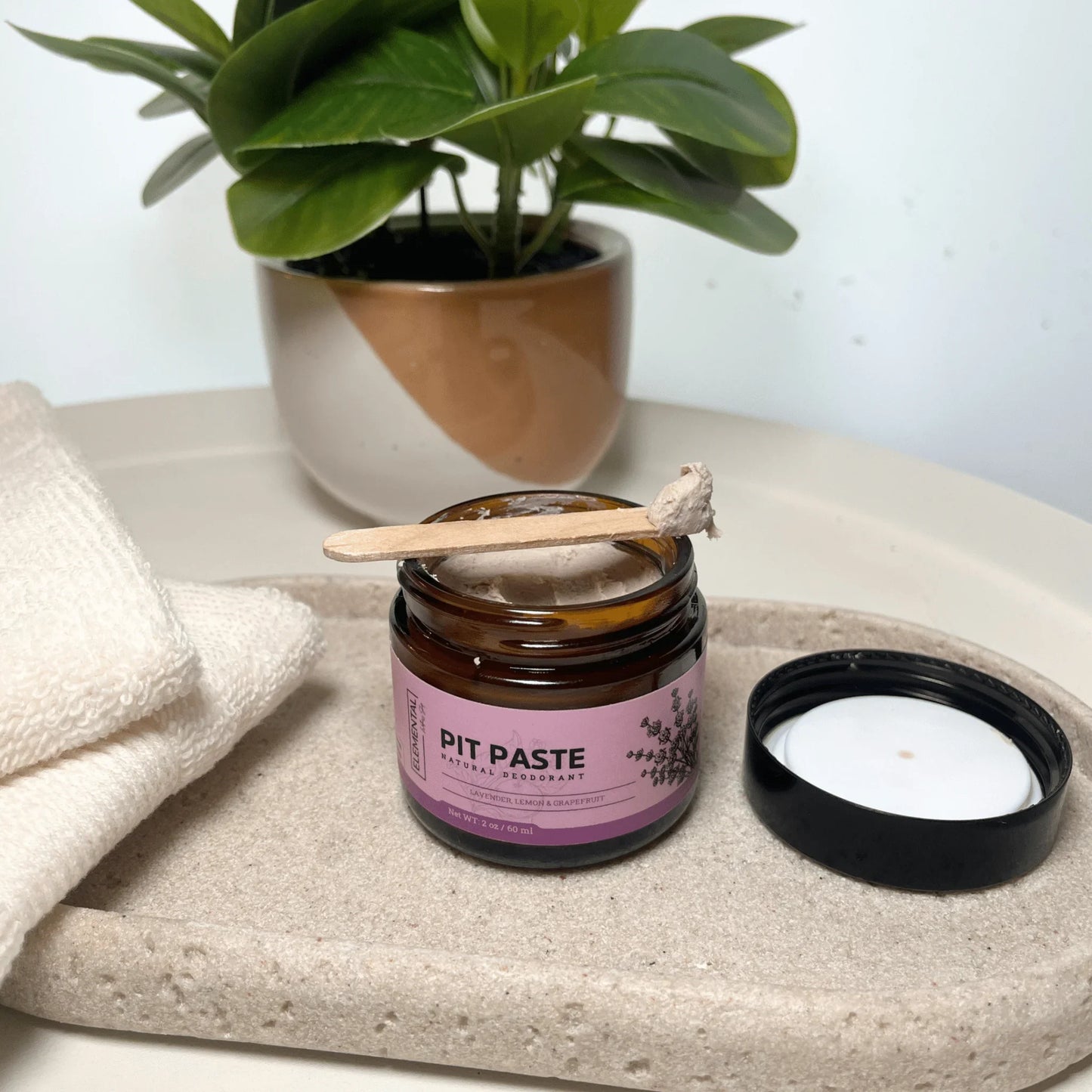 Pit Paste all natural deodorant jar with lid, wooden applicator, and towel on a tray