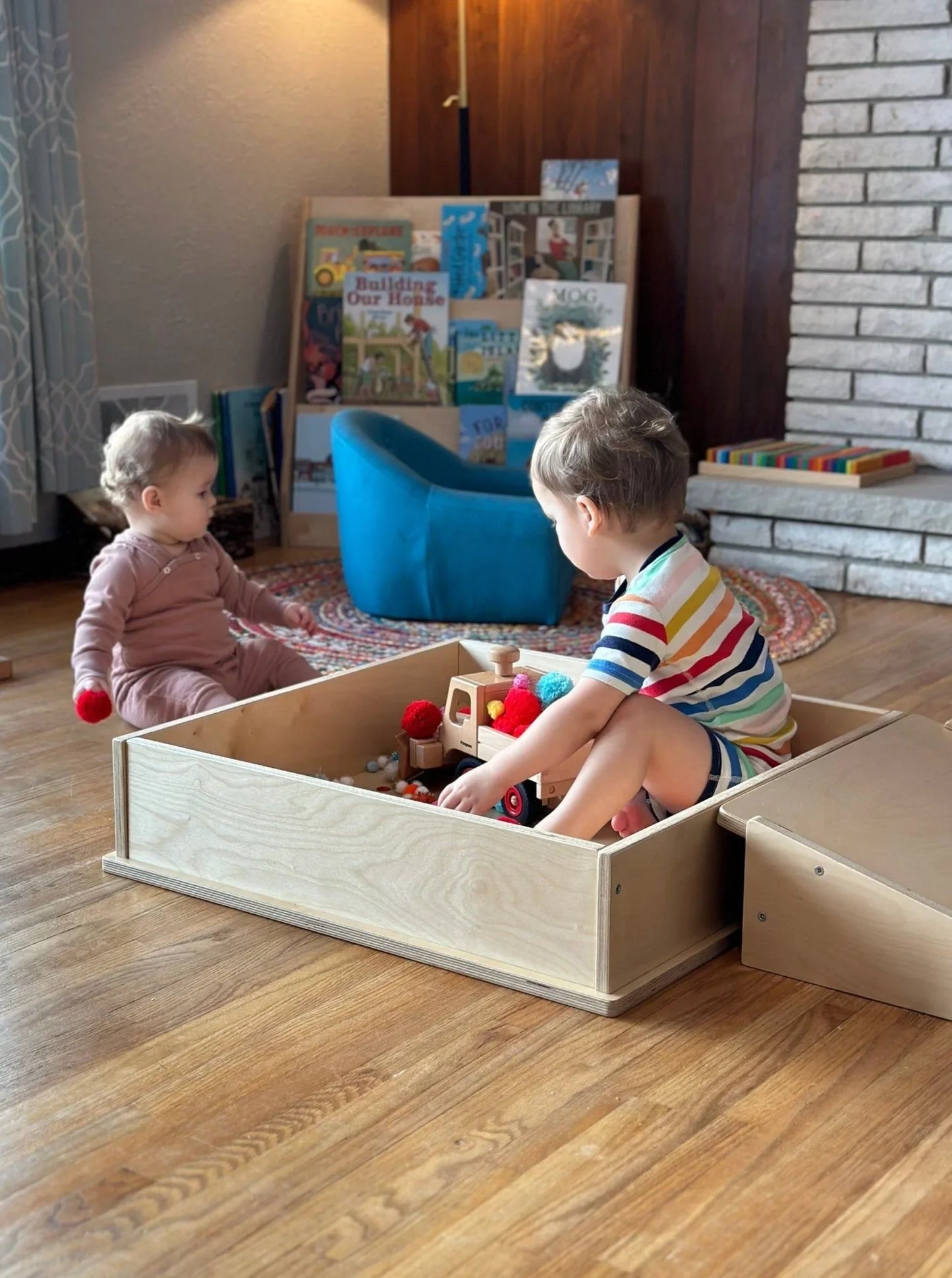 Two young children playing with sensory toys in a wooden sensory play box indoors