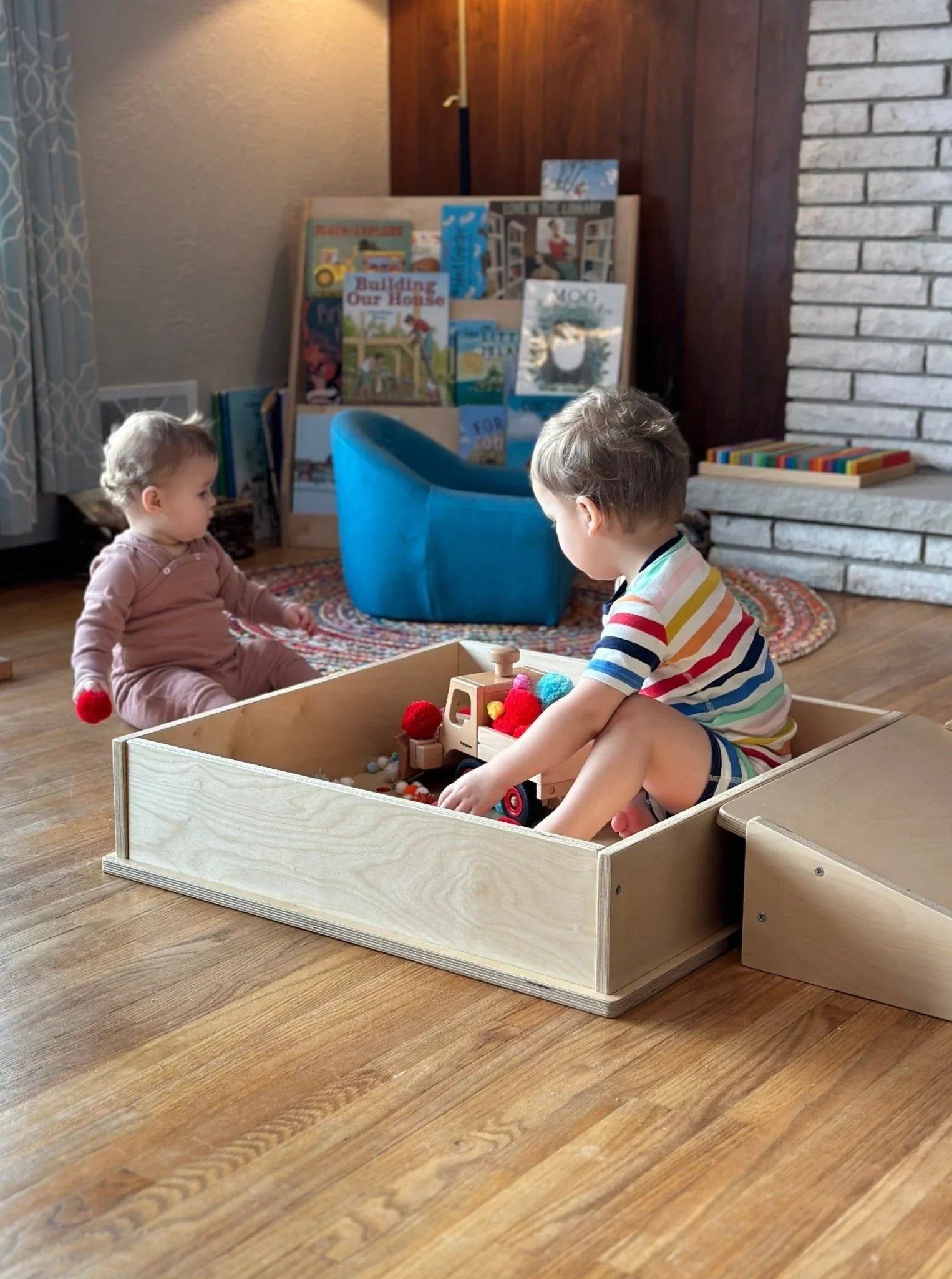 Two young children playing with sensory toys in a wooden sensory play box indoors