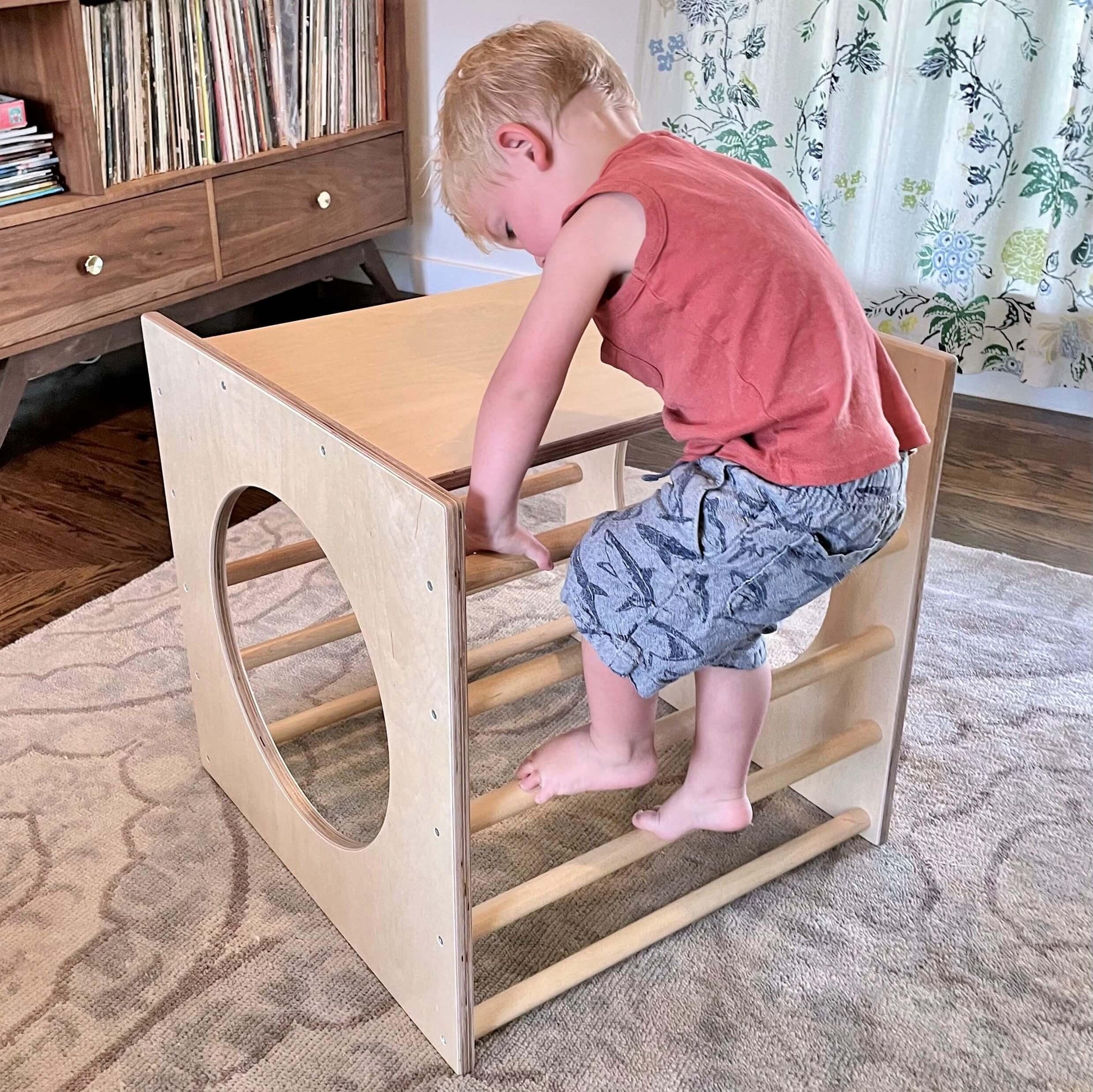 Toddler climbing on a wooden Montessori play cube in a sensory-friendly room