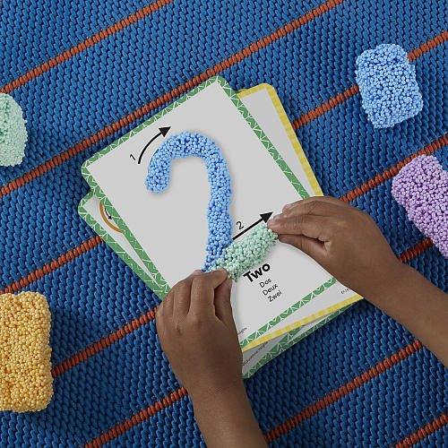 Child shaping foam modeling beads into the number two on a textured learning card on a blue mat