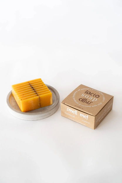 Natural probiotic bar soap with yellow-orange color on a dish beside cardboard packaging on white background