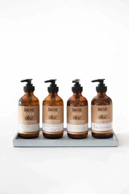 Four amber pump bottles of botanical liquid hand soap arranged neatly on a tray showcasing the different available scents.