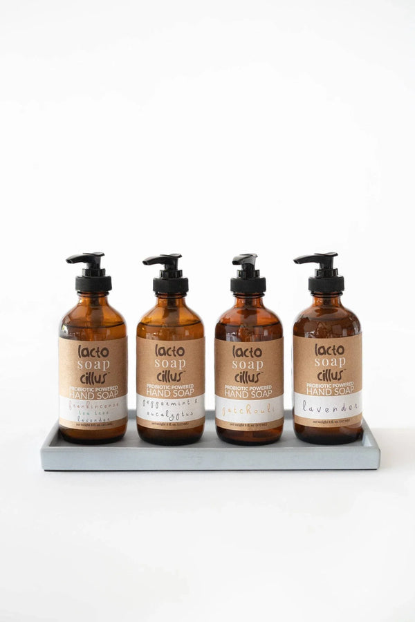Four amber pump bottles of botanical liquid hand soap arranged neatly on a tray showcasing the different available scents.