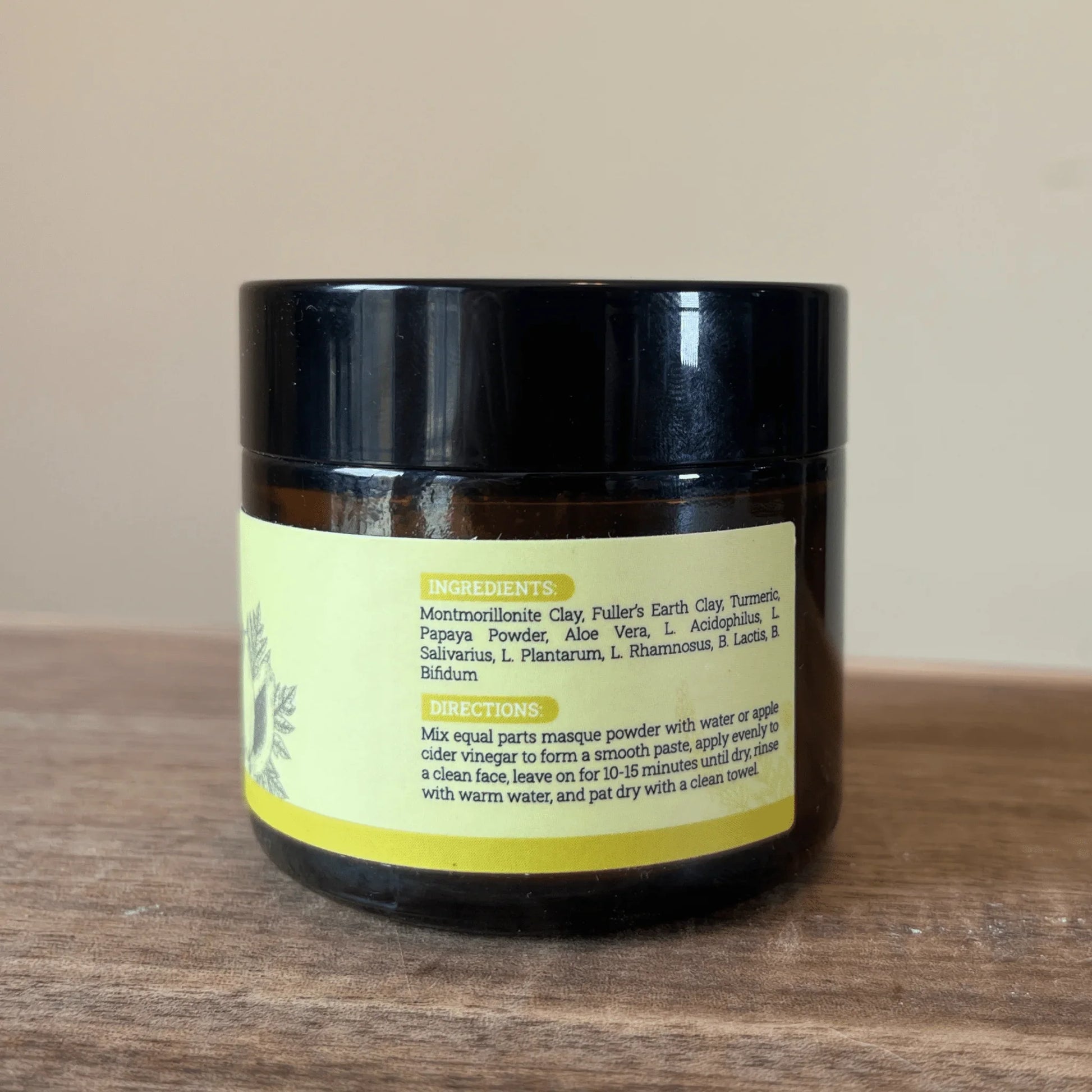 Brown jar of face mask powder with ingredient and directions label on wooden surface