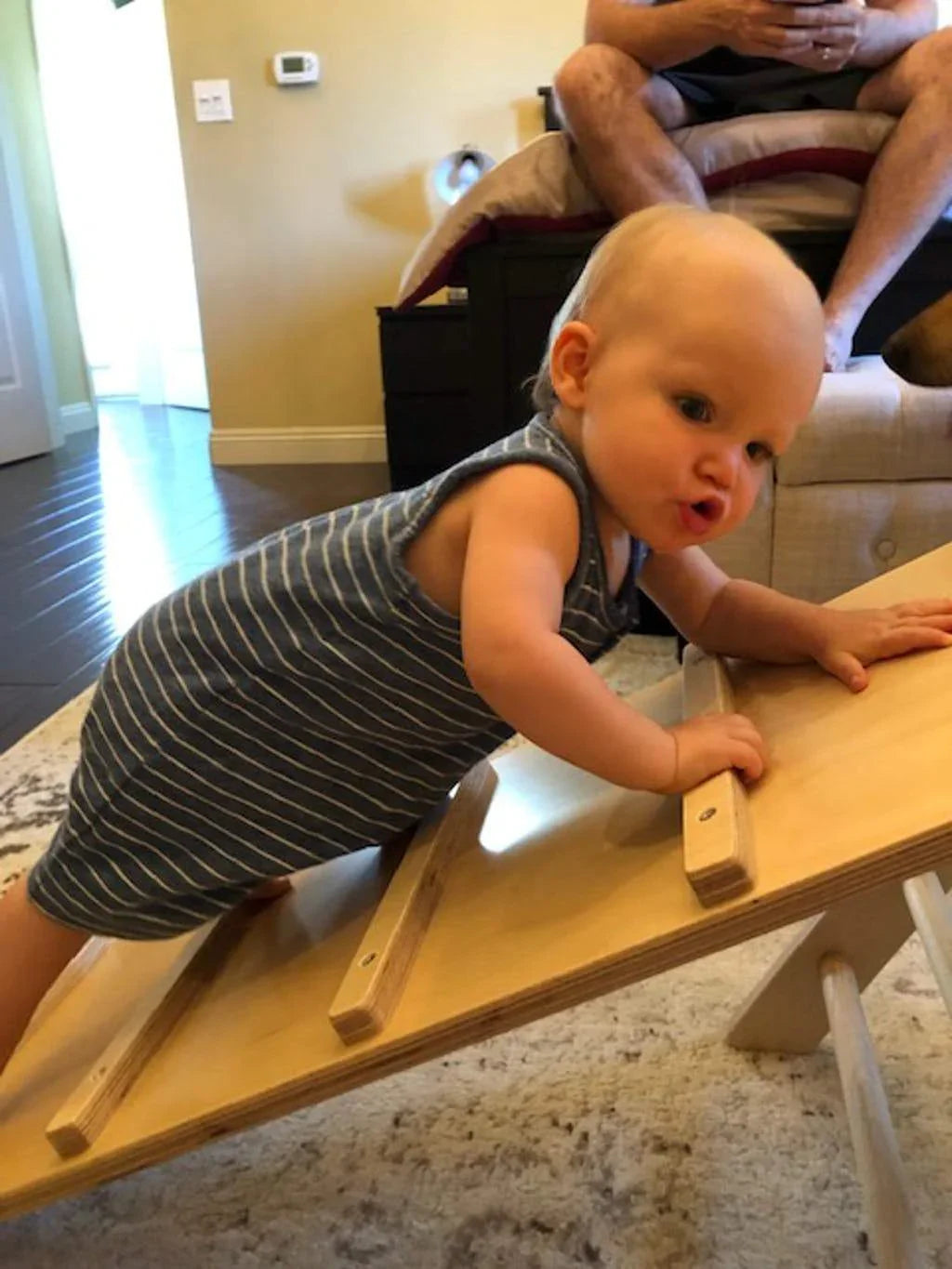 Baby climbing on a wooden reversible sensory climbing ramp indoors