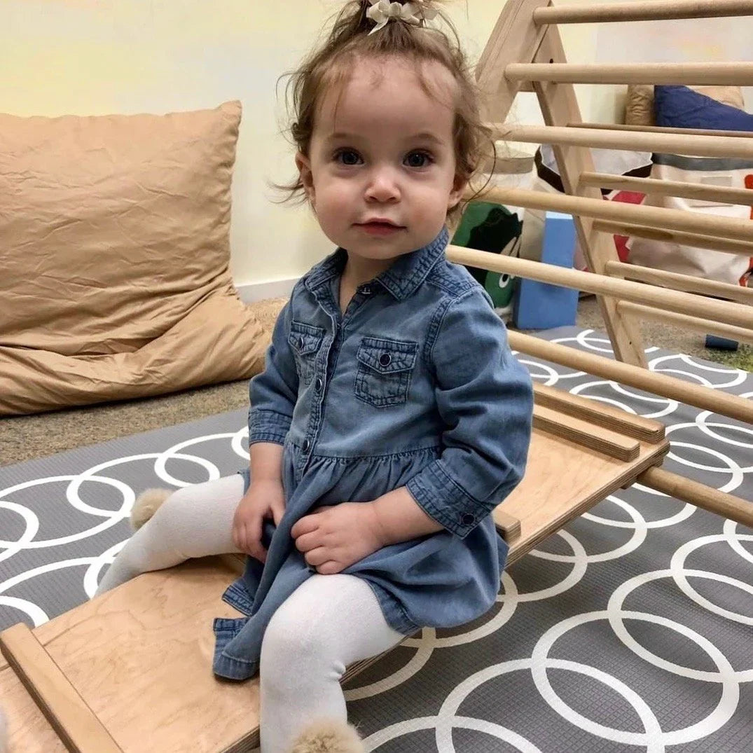 Young child sitting on a wooden reversible climbing ramp for sensory play indoors