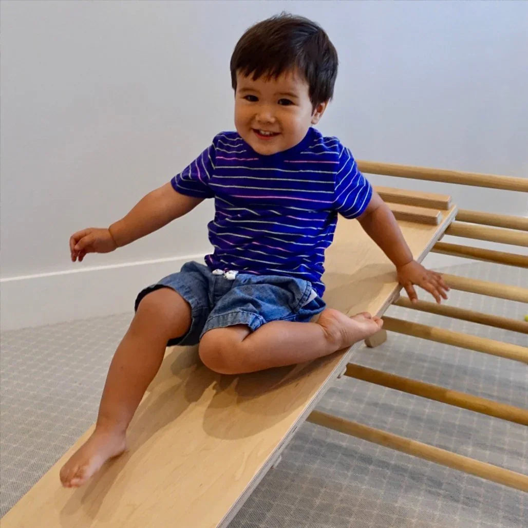 Young child playing on a wooden reversible climbing ramp in a sensory-friendly room