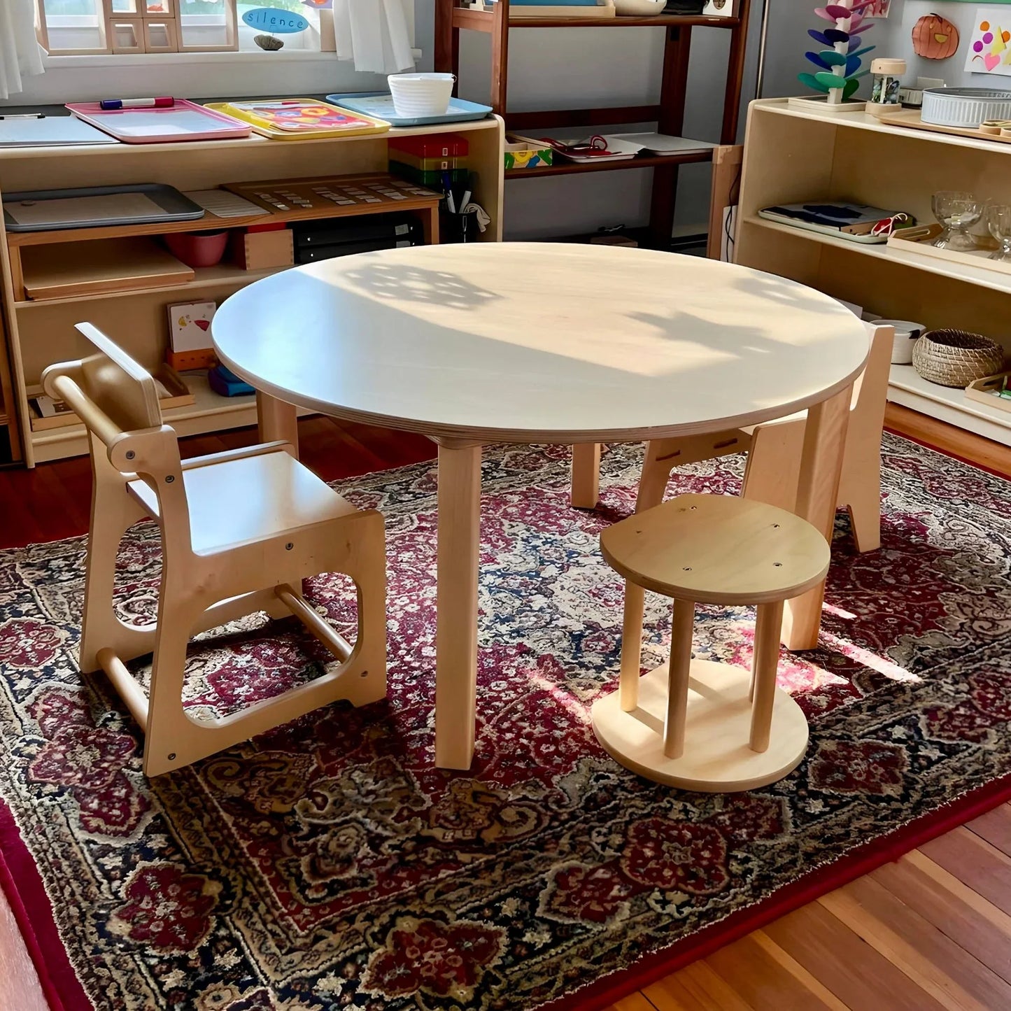 Montessori classroom with wooden table and chairs on patterned rug, sensory learning tools nearby