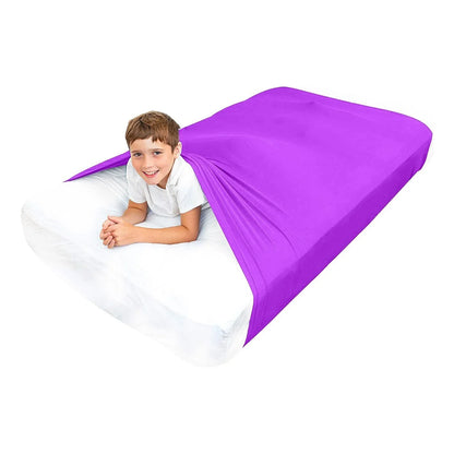 Child in white shirt under purple sensory compression sheet on a bed, sensory sleep aid