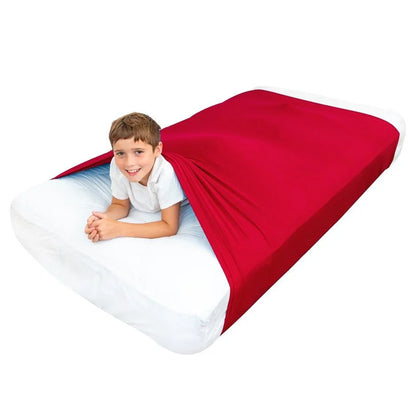 Child smiling inside red sensory compression sheet on a bed, sensory sleep aid for kids.