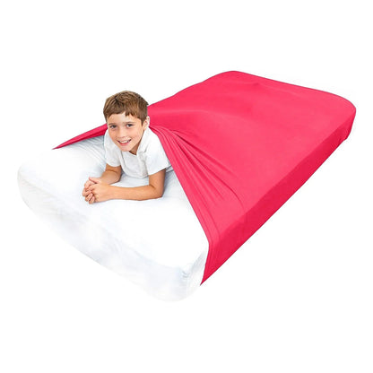 Child smiling under red sensory compression sheet on a bed, sensory-friendly sleep aid