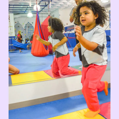 Child in sensory-friendly pants running in indoor play gym with colorful mats and swings