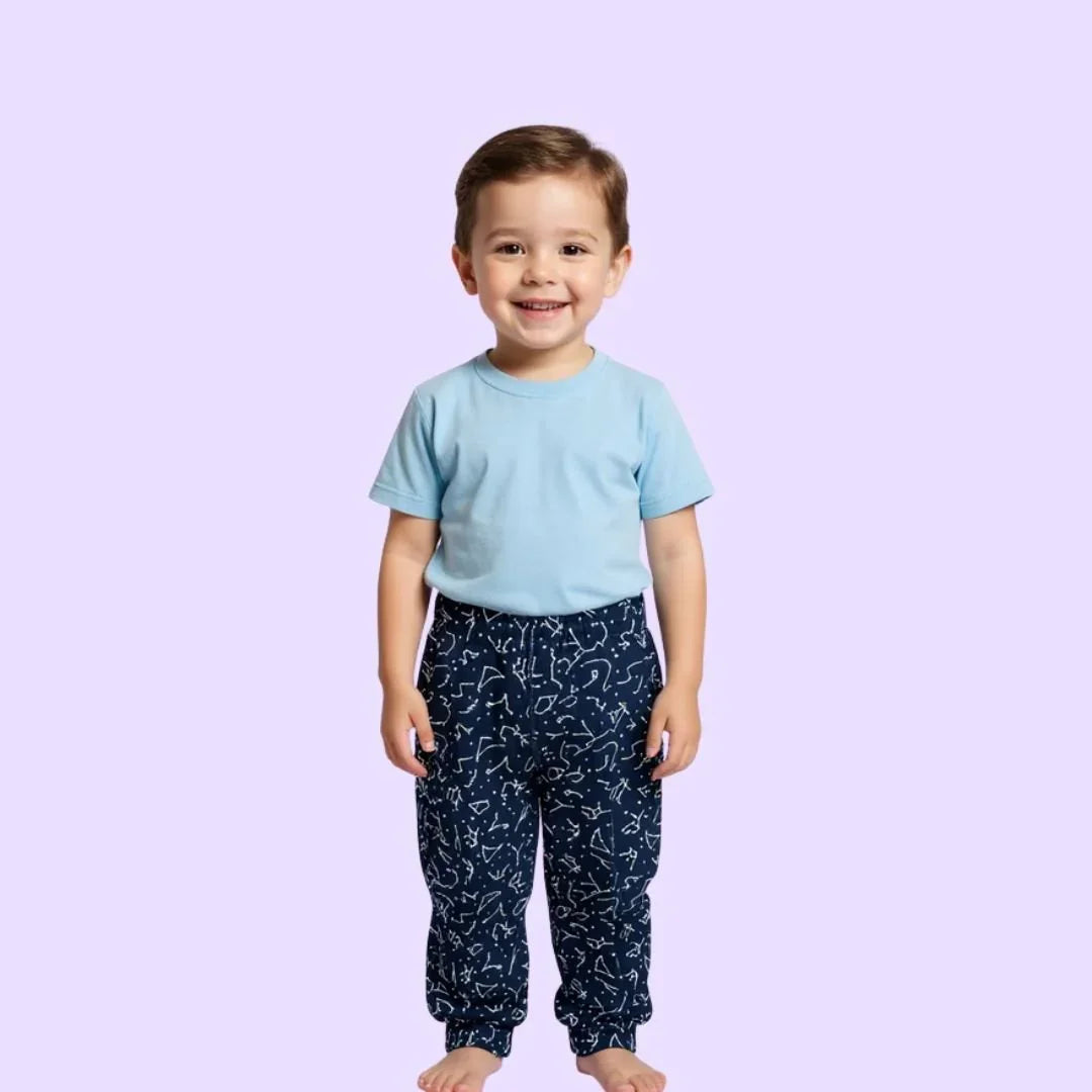 Young child in light blue sensory-friendly shirt and navy pattern pants, smiling on lavender background