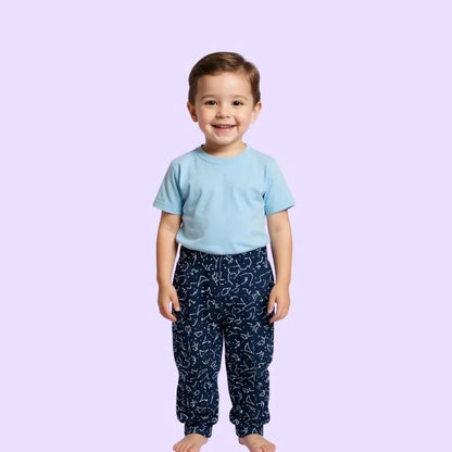 Young child in light blue sensory-friendly shirt and navy pattern pants, smiling on lavender background