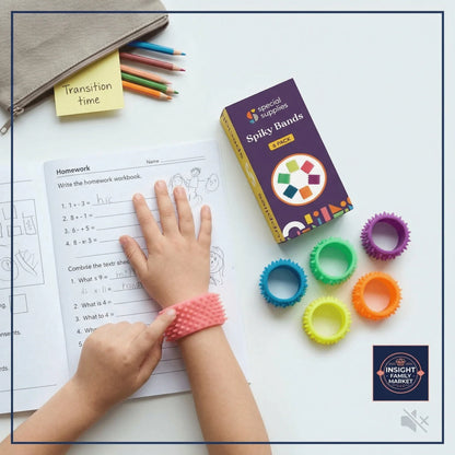 Child wearing spiky band while doing homework, with colorful fidget bands nearby.