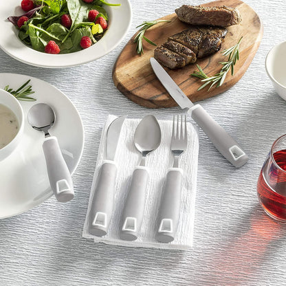 Adaptive utensils with thick gray handles on a table set with salad, steak, soup, and a drink