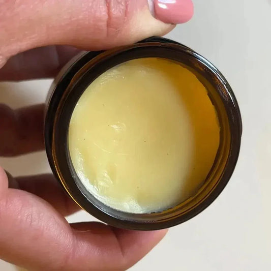 Hand holding open jar of yellow skin healing salve for dry or cracked skin