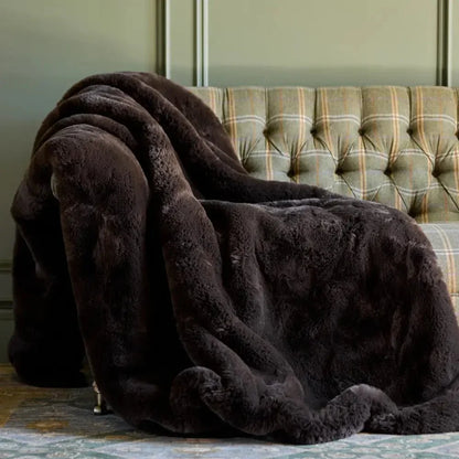 Plush mocha faux fur blanket draped over a green plaid tufted sofa