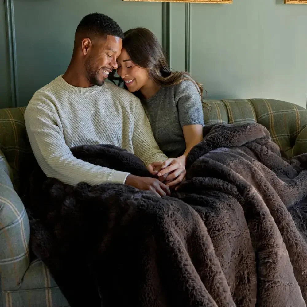 Smiling couple cuddling under a plush mocha sensory blanket on a sofa