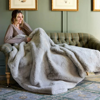 Woman relaxing under a plush grey sensory blanket on a sofa in a cozy living room.