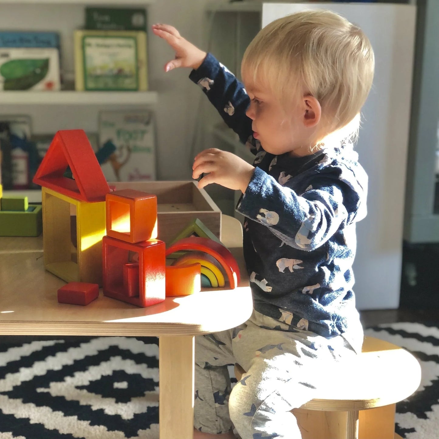 Toddler playing with wooden sensory blocks at a light wood sensory table in a playroom