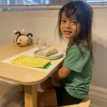 Child in green shirt sits at a table with a wrap, yellow napkin, and plush bee toy nearby