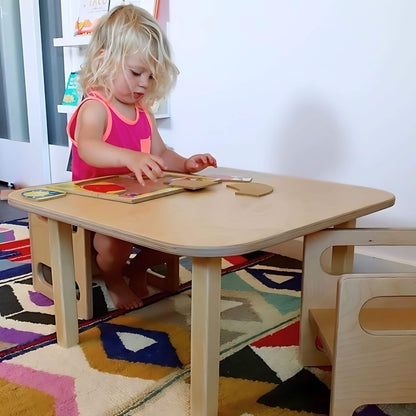 Toddler playing with puzzle at Montessori toddler table on colorful sensory rug.