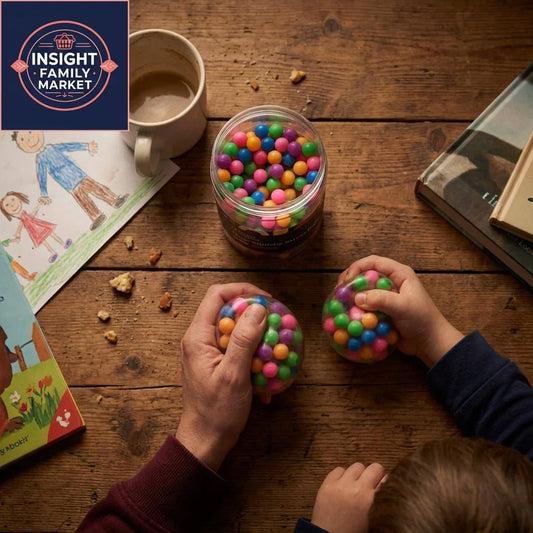 Parent and child holding colorful sensory stress balls at a wooden table with books and drawing.