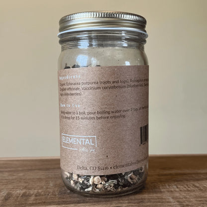 Glass jar of loose leaf herbal tea with brown label showing organic ingredients and instructions.